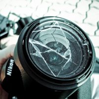 A cracked camera lens with motes of dust on it, against the backdrop of a cobbled stone road.